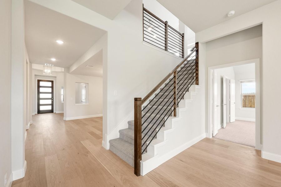Open foyer with staircase featuring wood and metal railing, light hardwood floors, and front entry door visible in background. Open foyer with staircase featuring wood and metal railing, light hardwood floors, and front entry door visible in background.