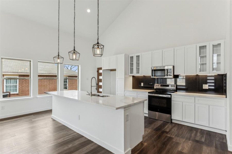 Kitchen with sink, appliances with stainless steel finishes, white cabinetry, hanging light fixtures, and an island with sink