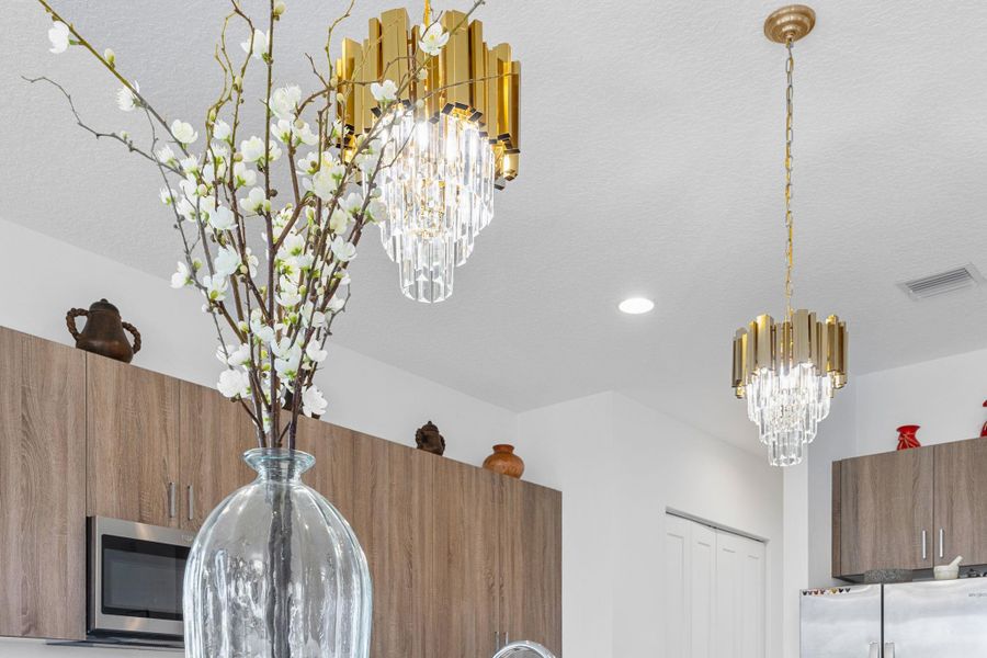 Kitchen view of brown cabinetry, a chandelier, refrigerator, stainless steel microwave, and modern cabinets