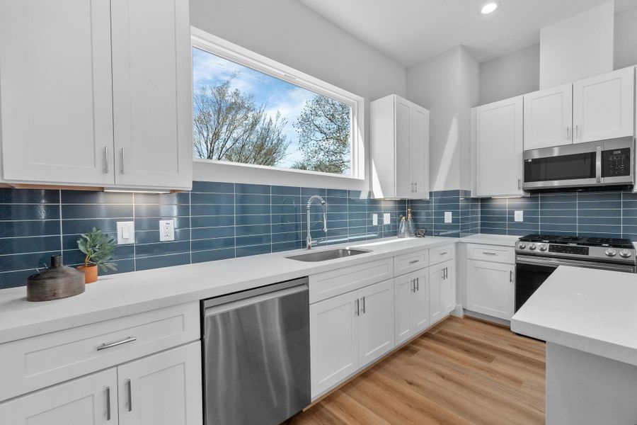 Designer kitchen featuring quartz countertops, shaker-style cabinetry, stainless steel appliances, and a sleek tile backsplash, all anchored by a large picture window for natural light.