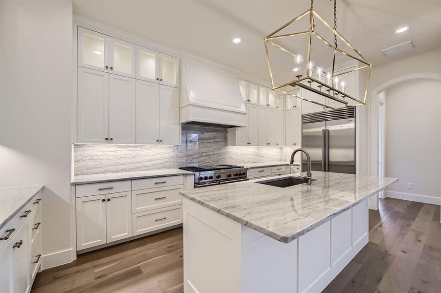 Kitchen with a center island with sink, sink, custom range hood, high end appliances, and dark wood-type flooring