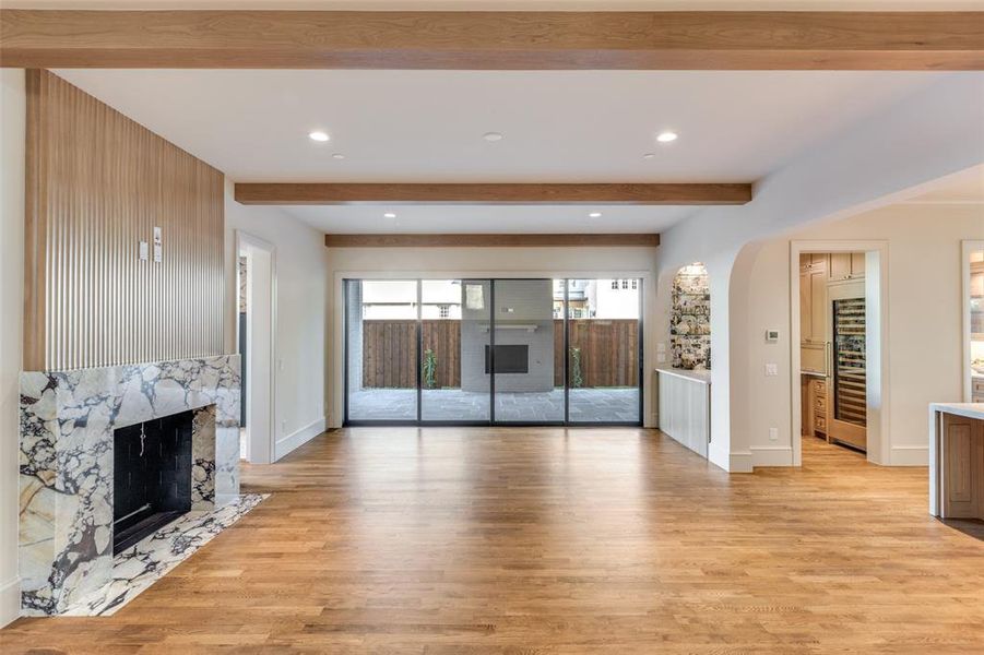 Unfurnished living room with a high end fireplace, light wood-style flooring, recessed lighting, beamed ceiling, and arched walkways Unfurnished living room with a high end fireplace, light wood-style flooring, recessed lighting, beamed ceiling, and arched walkways