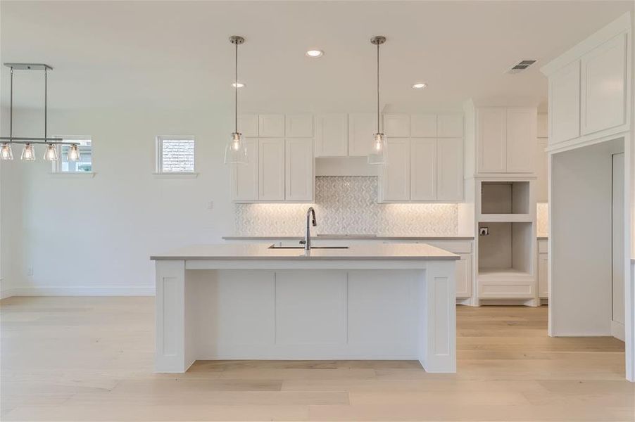 Kitchen featuring light hardwood / wood-style floors, white cabinetry, an island with sink, backsplash, and sink