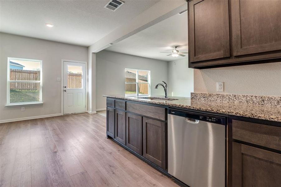 Kitchen featuring stainless steel dishwasher, a peninsula, light wood-type flooring, light stone countertops, and dark wood finish cabinetry