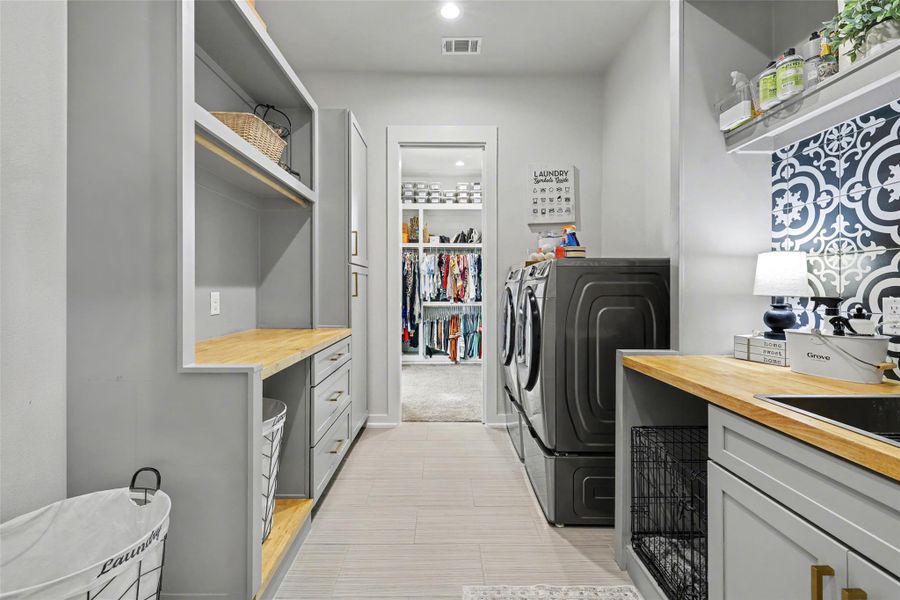 Laundry area featuring custom cabinetry, stainless sink, butcher bloc counter tops, pocket door and slider door goes to primary closet and hallway entrance to primary suite