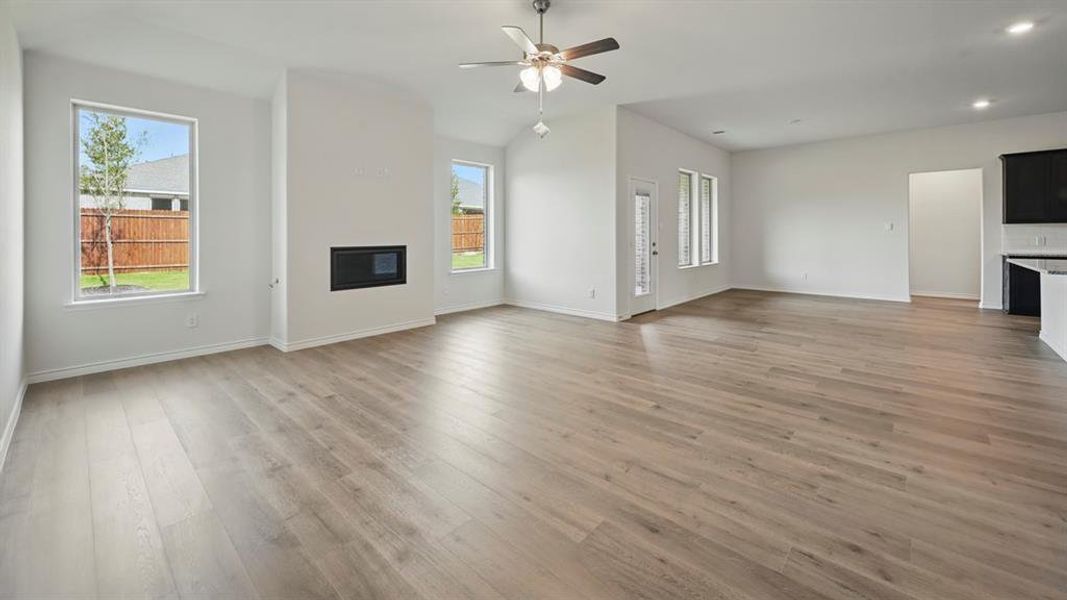 Unfurnished living room with a glass covered fireplace, light wood-style flooring, a ceiling fan, recessed lighting, and vaulted ceiling