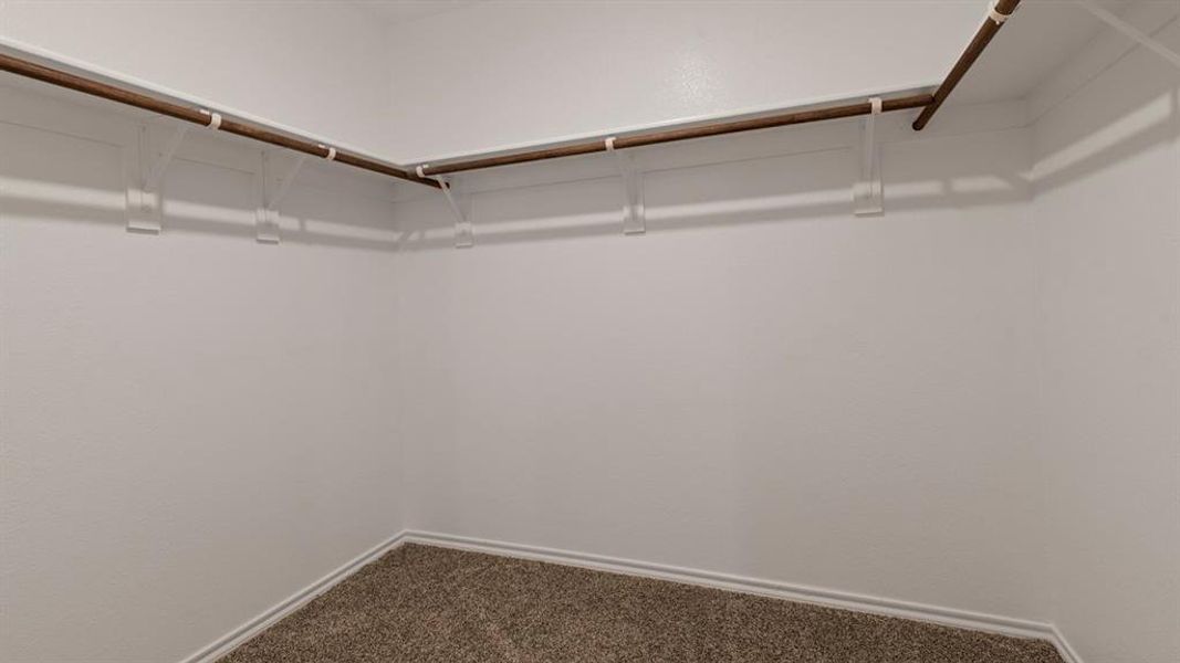 Spacious walk-in closet featuring white walls, corner shelving, and built-in clothes rods Spacious walk-in closet featuring white walls, corner shelving, and built-in clothes rods