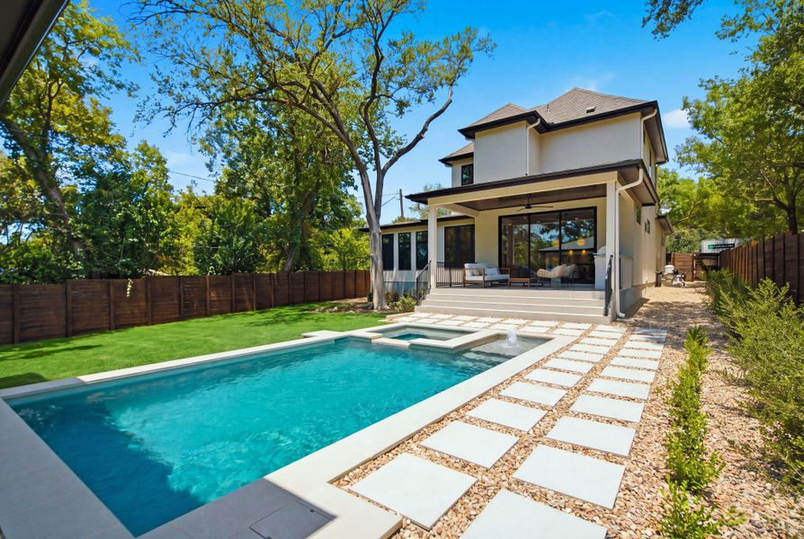 An inviting backyard oasis features a geometric pool, stone paver decking, and manicured lawn.