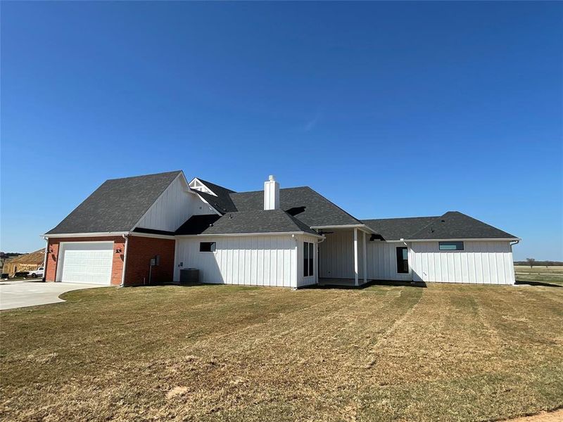 Side view exterior with a chimney, a lawn, an attached garage, roof with shingles, and concrete driveway