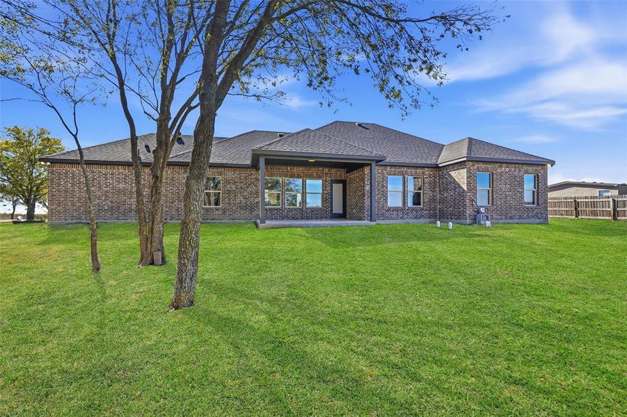 Back of property with a yard, a patio area, brick siding, and roof with shingles