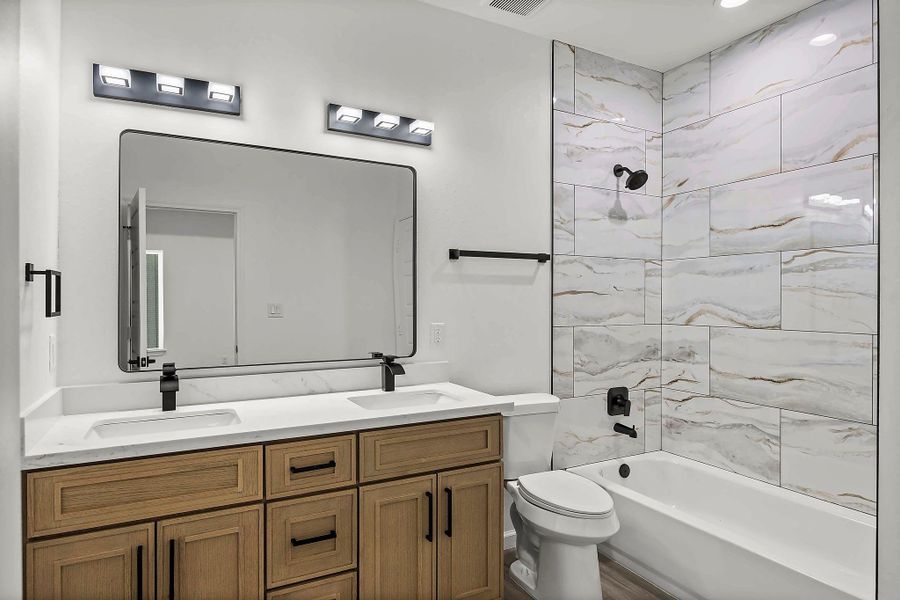 Modern bathroom featuring a sleek double vanity with dark fixtures, elegant marble-tiled shower, and warm wood cabinetry for a touch of luxury.