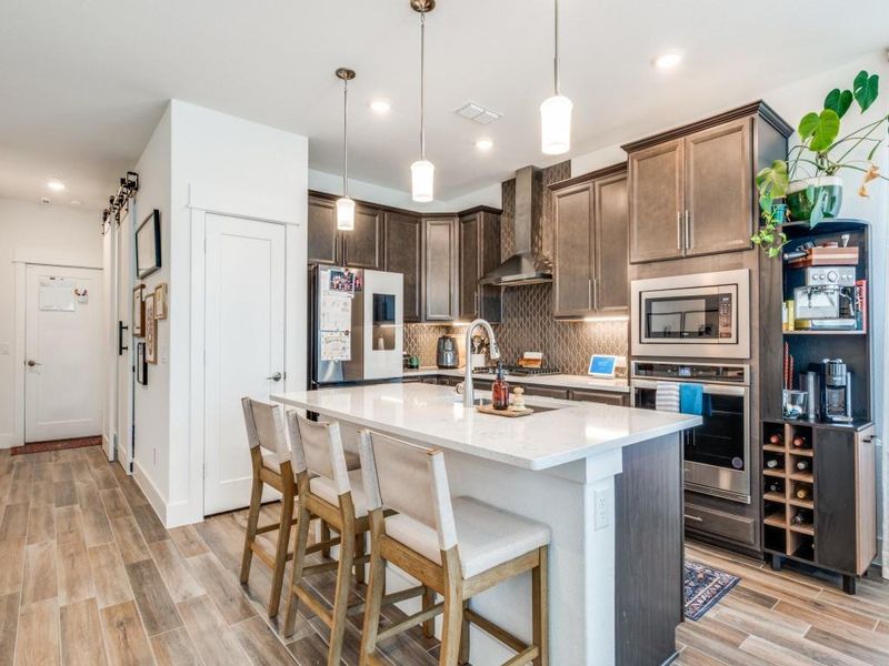 Kitchen with appliances with stainless steel finishes, wall chimney exhaust hood, decorative backsplash, light wood finished floors, and a breakfast bar
