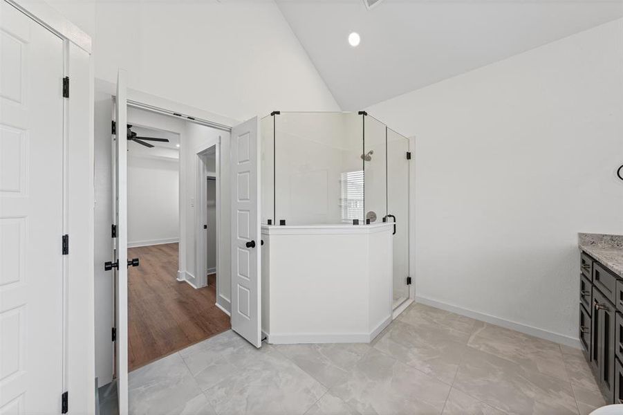A modern bathroom featuring a glass-enclosed shower, a vanity with a stone countertop, and light-colored tiled flooring