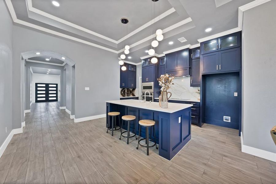 Kitchen featuring a central island with countertop seating, dark blue cabinetry, integrated stainless steel appliances, marble-look backsplash, and a contemporary pendant light fixture