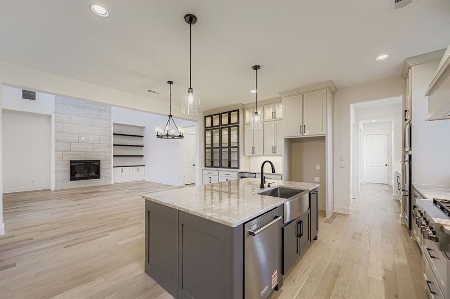 Kitchen with an island with sink, decorative light fixtures, light stone counters, light wood finished floors, and white cabinetry