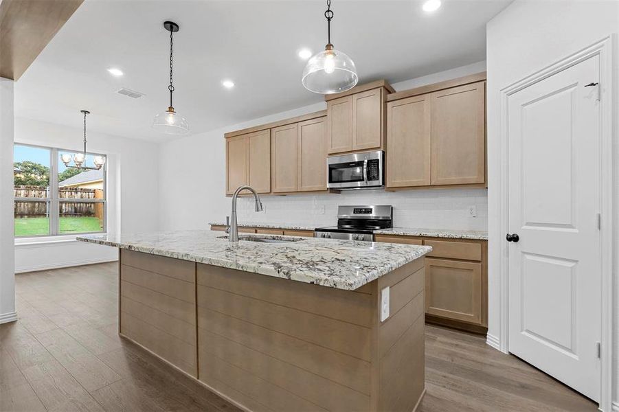 Kitchen featuring appliances with stainless steel finishes, light brown cabinets, hardwood / wood-style floors, sink, and a kitchen island with sink