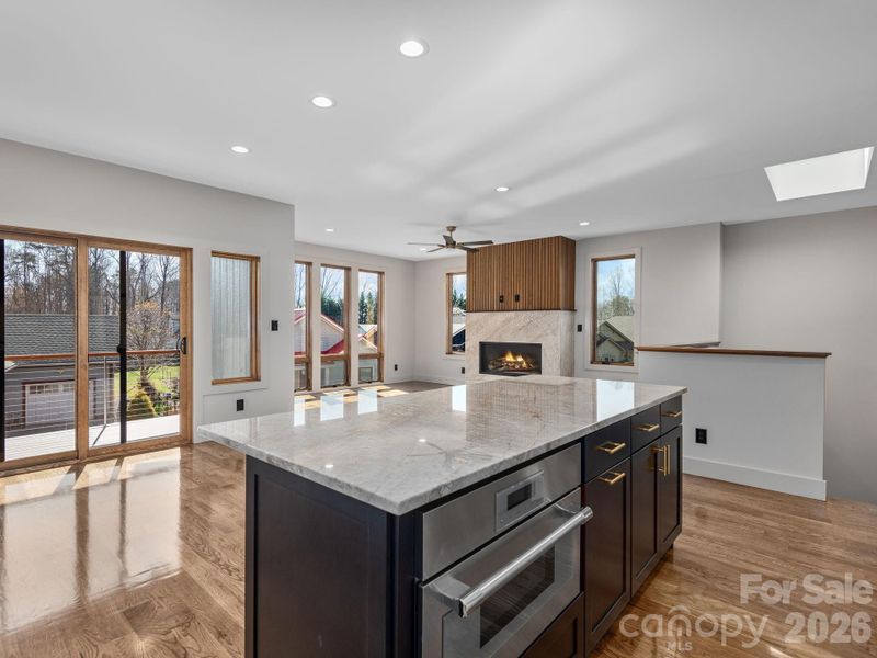 Representative photo from 50 Verde Drive showing the builder’s quality of construction and finish level, including the oversized kitchen island, oak hardwood floors, vented gas fireplace, and sliding doors opening to the covered deck.
