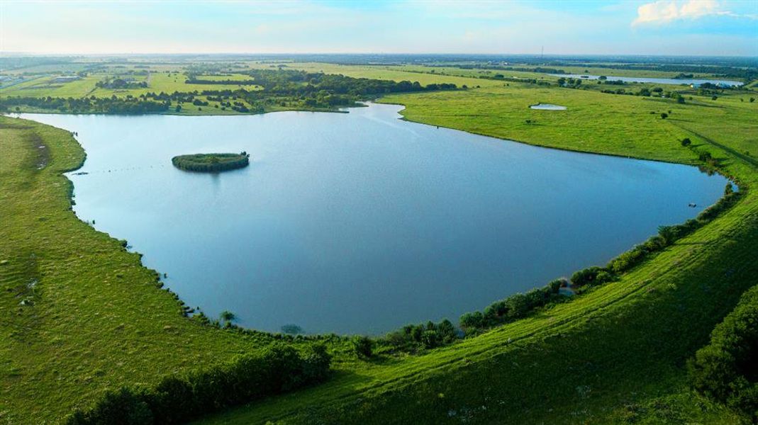 Expansive lake surrounded by rolling green hills and distant fields Expansive lake surrounded by rolling green hills and distant fields