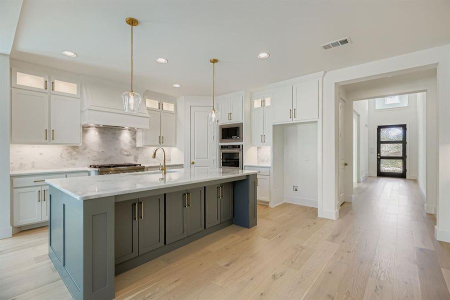 Kitchen featuring glass insert cabinets, decorative backsplash, decorative light fixtures, white cabinetry, and light wood-style floors Kitchen featuring glass insert cabinets, decorative backsplash, decorative light fixtures, white cabinetry, and light wood-style floors