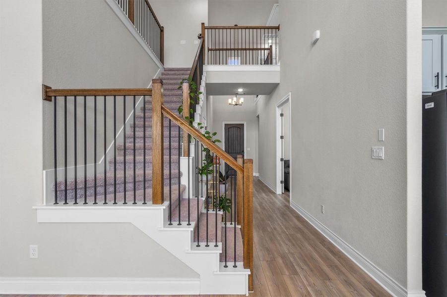An open entryway leads past a carpeted staircase with wood handrails to a long hallway.
