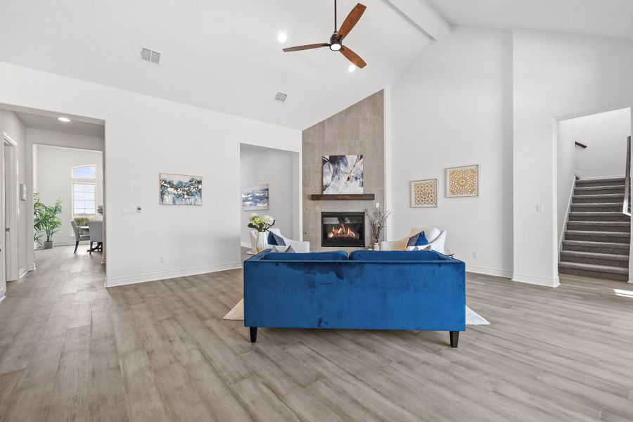 Living room with a ceiling fan, beamed ceiling, stairway, a tiled fireplace, and high vaulted ceiling