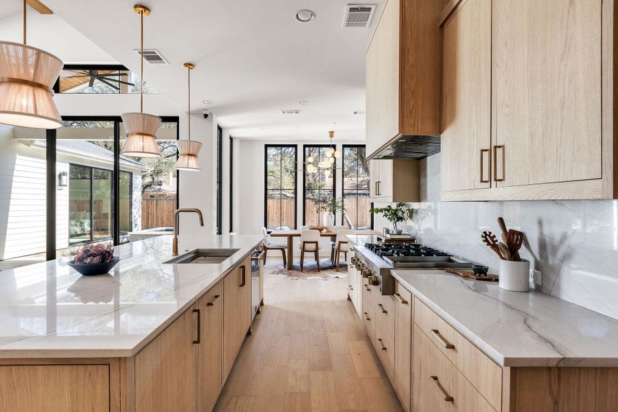 Kitchen featuring light wood finish cabinets, light stone counters, a large island, and pendant lighting
