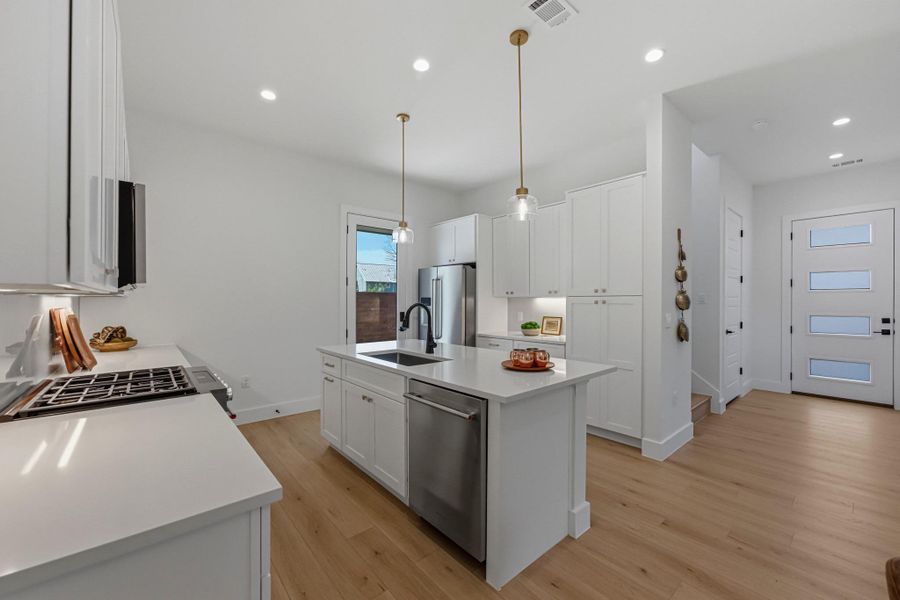 Kitchen with white cabinetry, stainless steel appliances, light wood-style flooring, and an island with sink