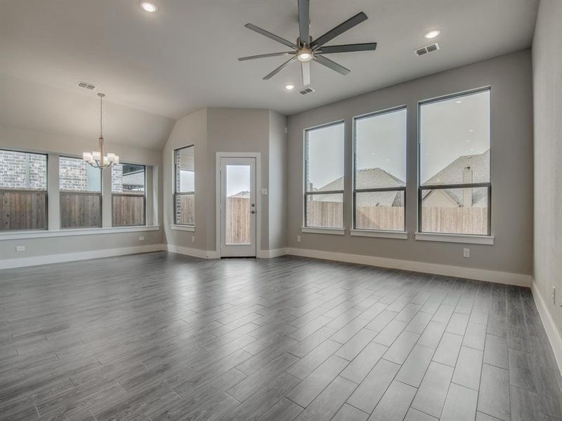 Unfurnished living room with a wealth of natural light, visible vents, dark wood finished floors, and ceiling fan with notable chandelier Unfurnished living room with a wealth of natural light, visible vents, dark wood finished floors, and ceiling fan with notable chandelier