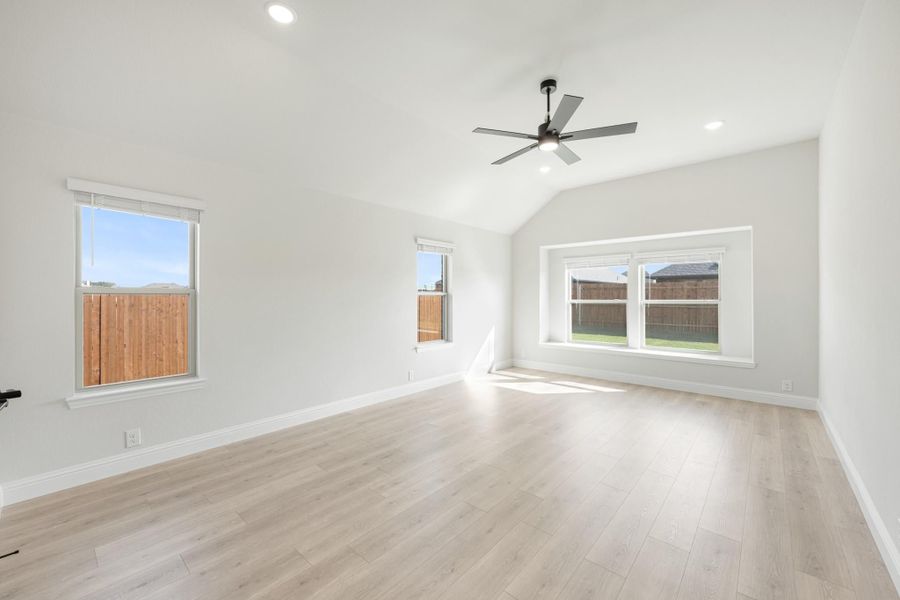 Empty bedroom with vaulted ceiling, ceiling fan, light wood floors, and multiple windows