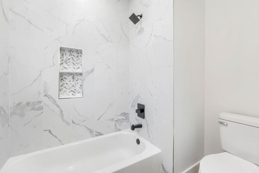 A pristine bathroom featuring sleek marble-patterned tile, a bathtub, and a modern shower with matte black fixtures.