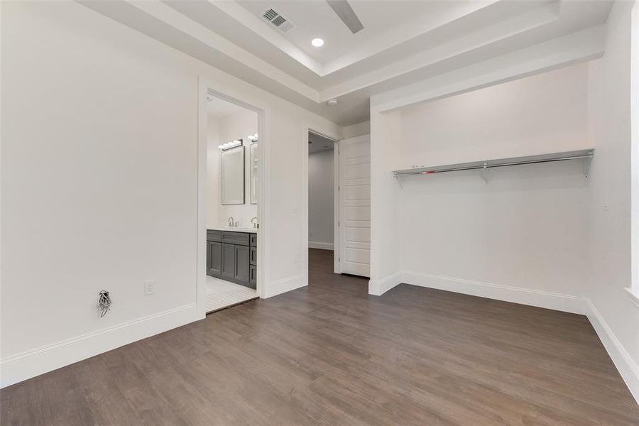 Unfurnished bedroom featuring ceiling fan, a raised ceiling, a closet, dark hardwood / wood-style floors, and ensuite bath