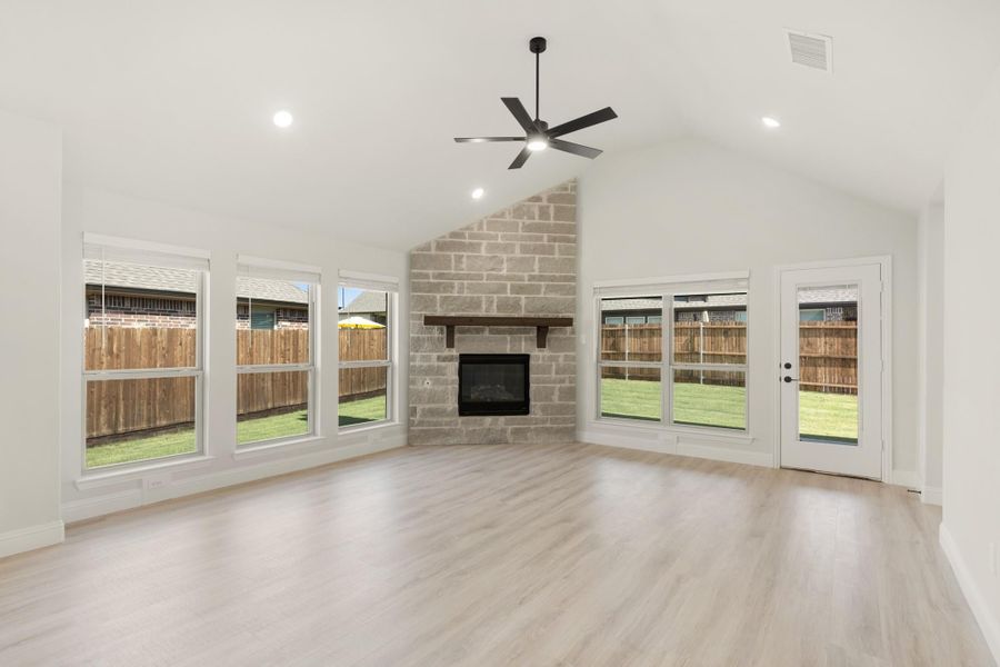 Open living room with vaulted ceiling, stone fireplace, ceiling fan, and light wood floors