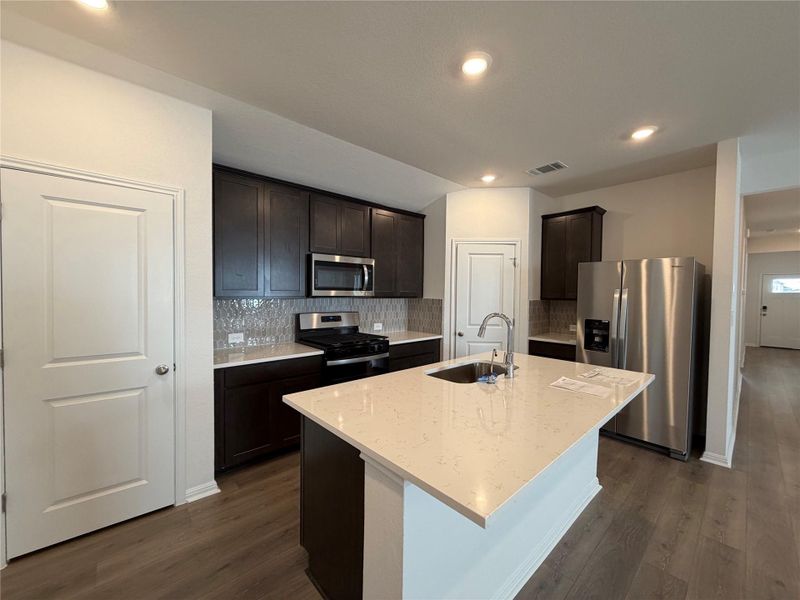 Kitchen featuring tasteful backsplash, appliances with stainless steel finishes, dark brown cabinets, light stone counters, and dark wood finished floors Kitchen featuring tasteful backsplash, appliances with stainless steel finishes, dark brown cabinets, light stone counters, and dark wood finished floors