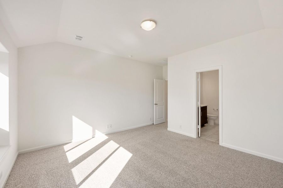 Empty bedroom with carpet flooring, white walls, and an open door leading to an ensuite bathroom