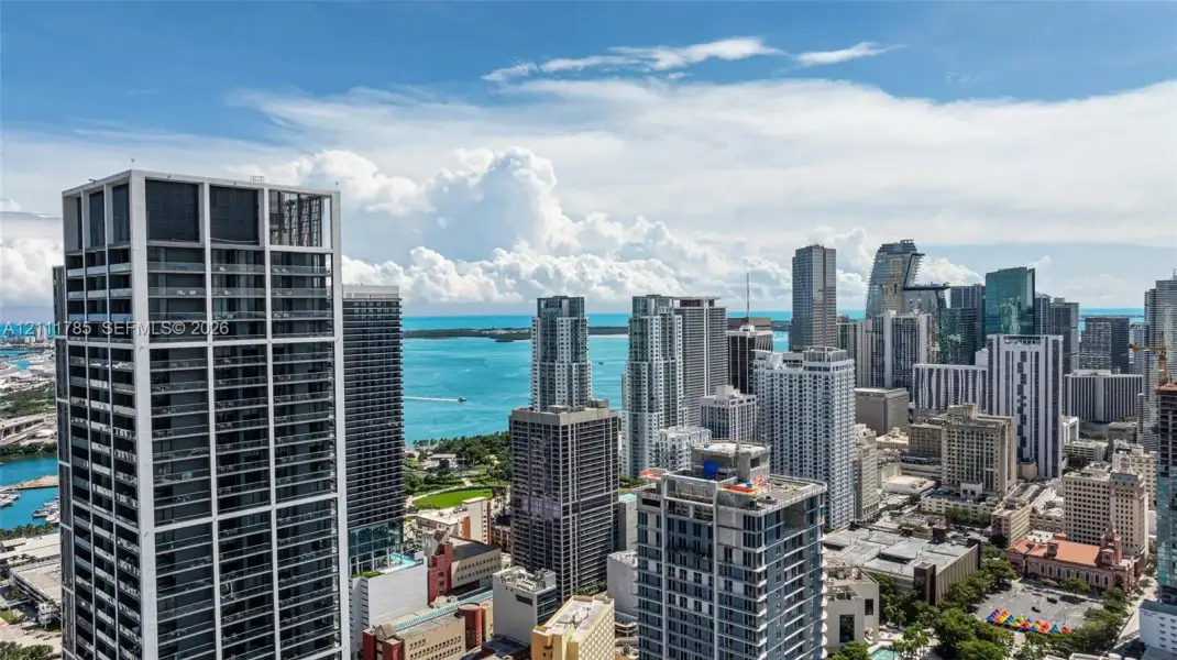 High-rise residential exterior with glass-panel balconies, featuring an expansive metropolitan skyline and coastal water backdrop