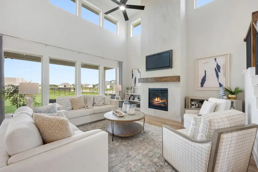 Living room with two-story ceiling, stone fireplace, ceiling fan, and large windows overlooking backyard Living room with two-story ceiling, stone fireplace, ceiling fan, and large windows overlooking backyard