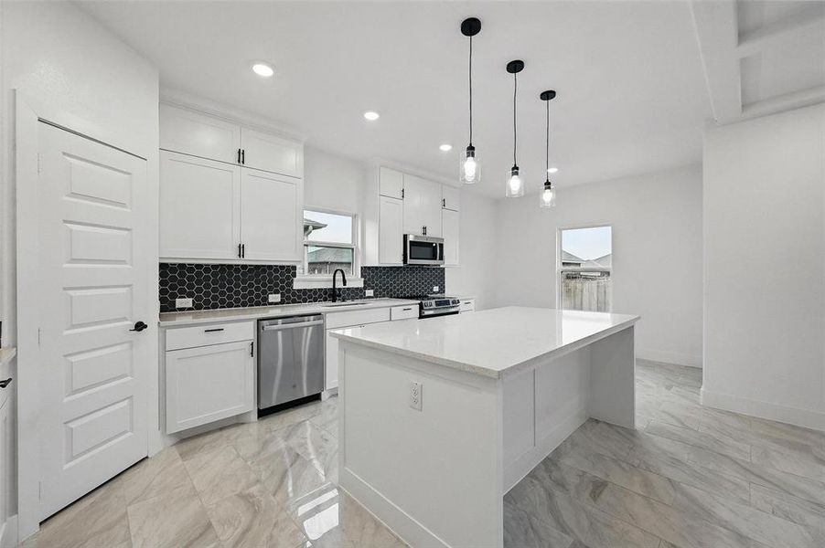 Kitchen with appliances with stainless steel finishes, light marble finish flooring, a center island, tasteful backsplash, and white cabinets