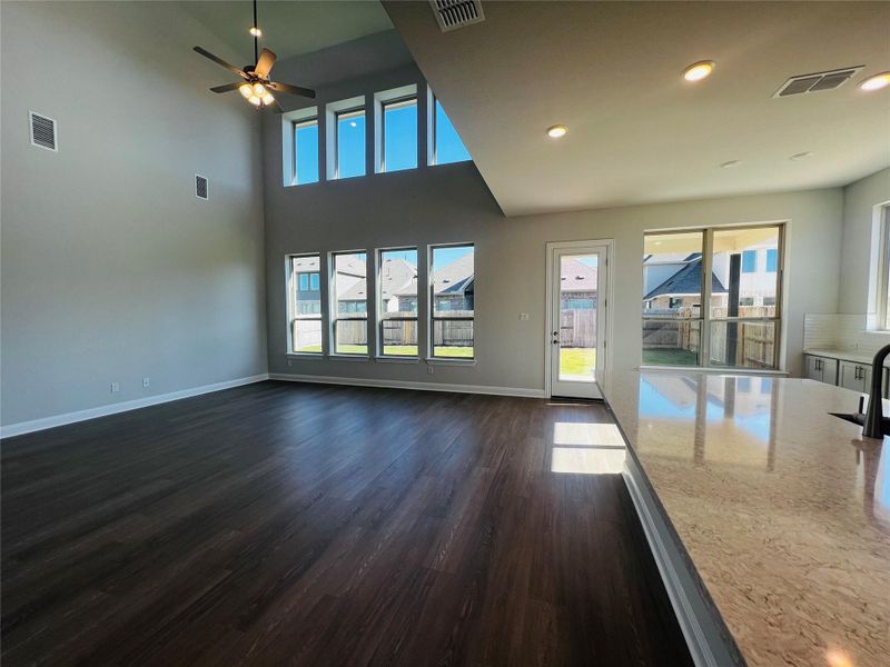 Unfurnished living room with dark wood-style flooring, ceiling fan, recessed lighting, and a towering ceiling