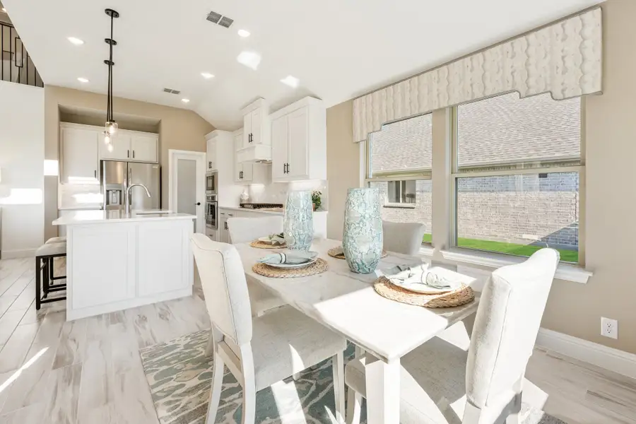 Dining area with white table and chairs open to kitchen with white cabinets and stainless steel appliances