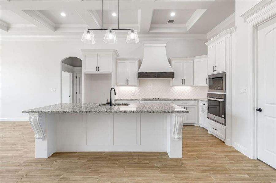 Kitchen featuring appliances with stainless steel finishes, custom exhaust hood, white cabinets, and an island with sink