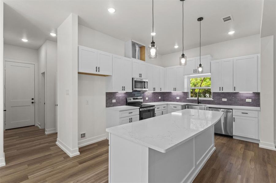 The kitchen features white cabinetry, a large kitchen island with a white countertop, and stainless steel appliances