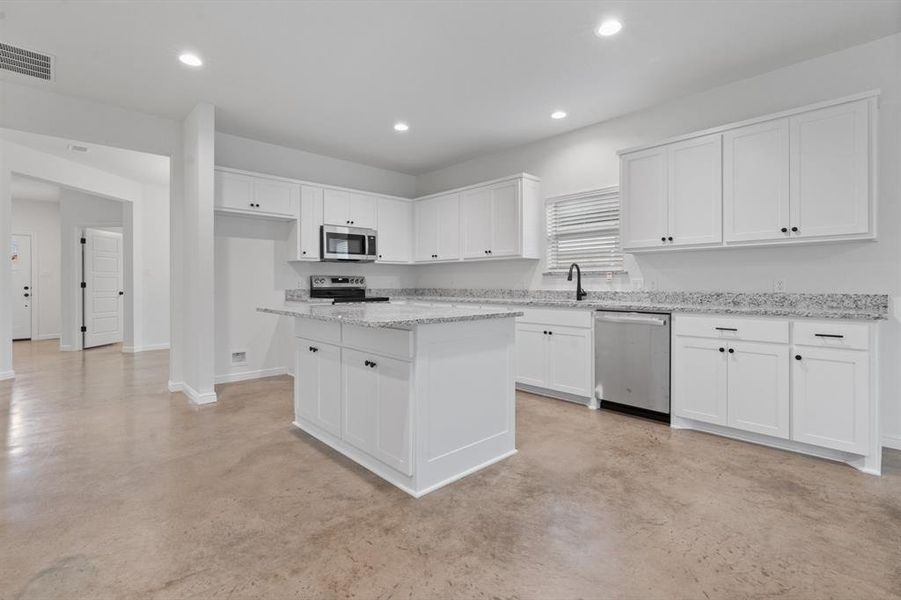 Kitchen featuring white cabinetry, stainless steel appliances, light stone counters, a center island, and sink