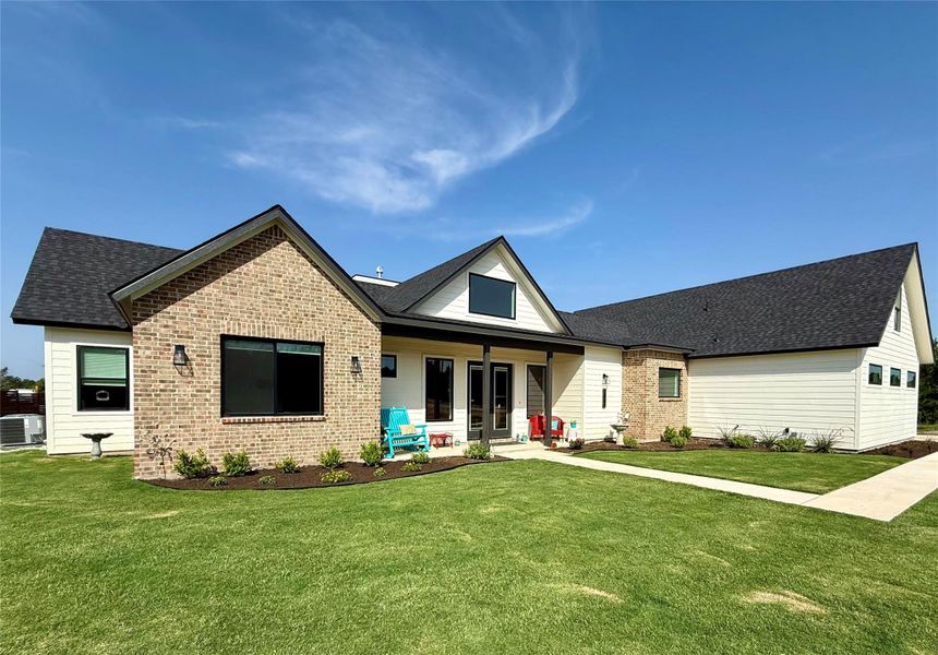 Rear view of house with brick siding, a yard, roof with shingles, and central air condition unit