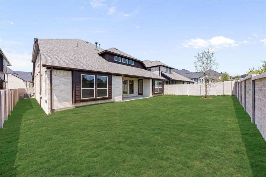 Rear view of brick home with covered patio, large fenced backyard, and green lawn