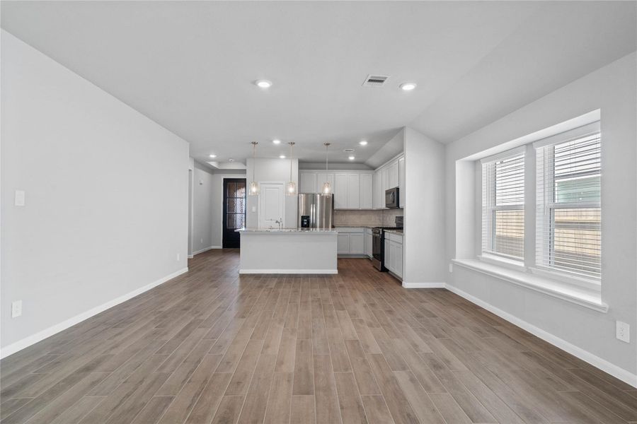 Enjoy meals in this sun-drenched space, featuring durable wood-look tile flooring, abundant natural light from the large windows (fitted with blinds), window seat, sloped ceiling, and recessed lighting.