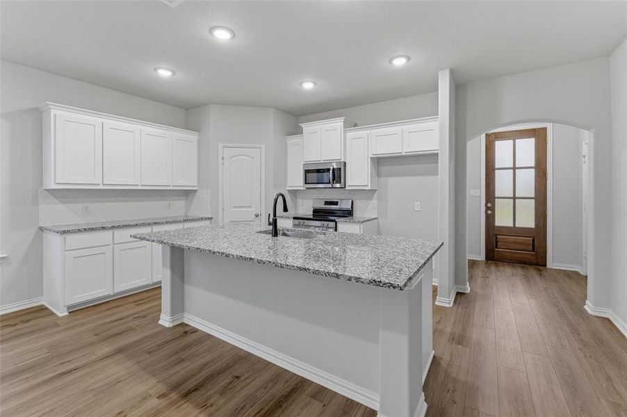 Kitchen featuring a large island with a sink, stainless steel appliances, white cabinetry, granite countertops, and wood-finish flooring Kitchen featuring a large island with a sink, stainless steel appliances, white cabinetry, granite countertops, and wood-finish flooring