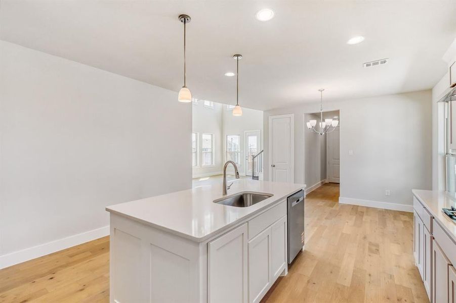 Kitchen with a kitchen island with sink, light wood-style flooring, white cabinetry, and hanging lights