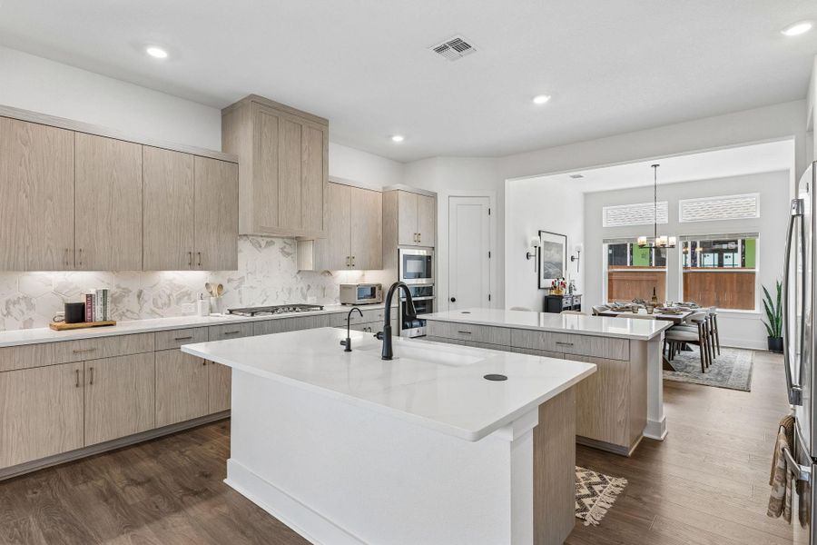 Plentiful counter space highlights this modern culinary space featuring dual islands and light wood cabinetry.