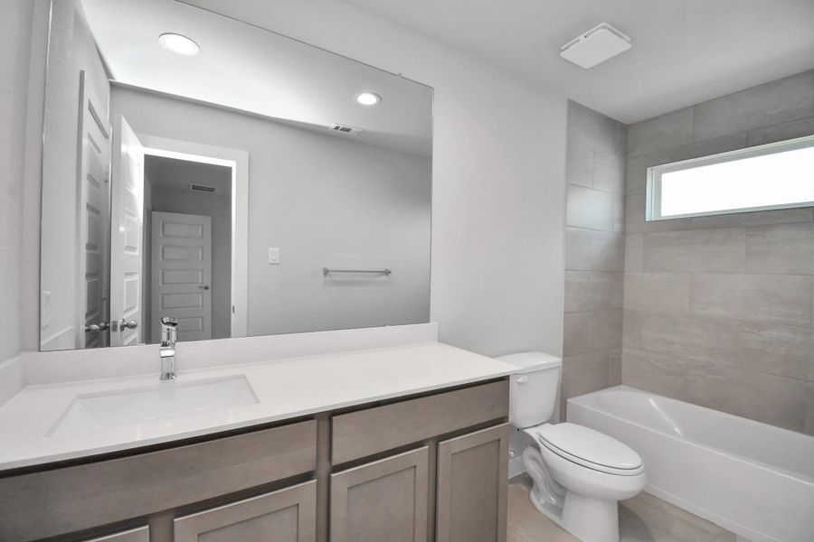 Secondary bath features tile flooring, bath/shower combo with tile surround, light stained wood cabinets, beautiful light countertop.