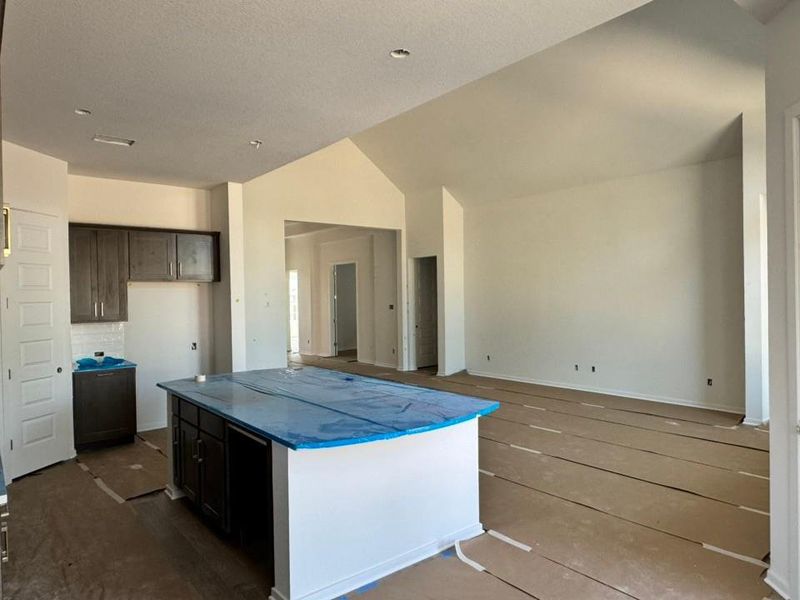 Kitchen featuring a kitchen island, vaulted ceiling, dark brown cabinetry, a textured ceiling, and open floor plan Kitchen featuring a kitchen island, vaulted ceiling, dark brown cabinetry, a textured ceiling, and open floor plan